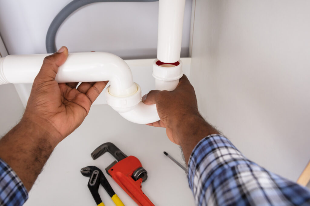 Close-up of plumber fitting sink pipe In residential kitchen